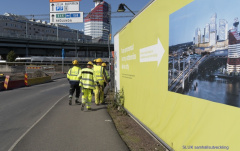 Byggarbetare är på väg till rast. Bakom dem finns en plansch hur det kommer att se ut när Hisingbron är klar.